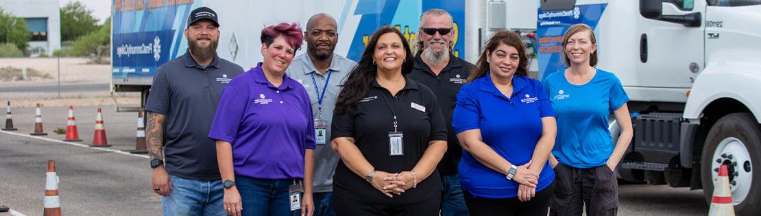 Pima's truck driving faculty and staff stand in front of a Pima truck posing for a photo